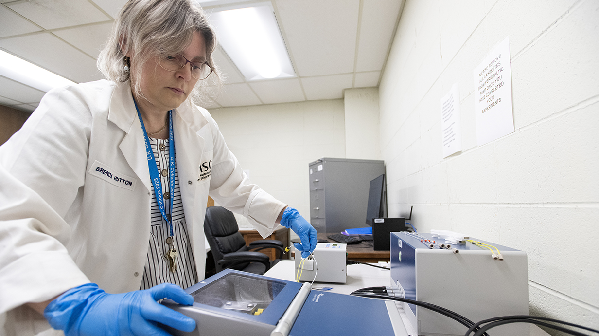 A woman wearing a white lab coat and blue gloves works with equipment in a laboratory.