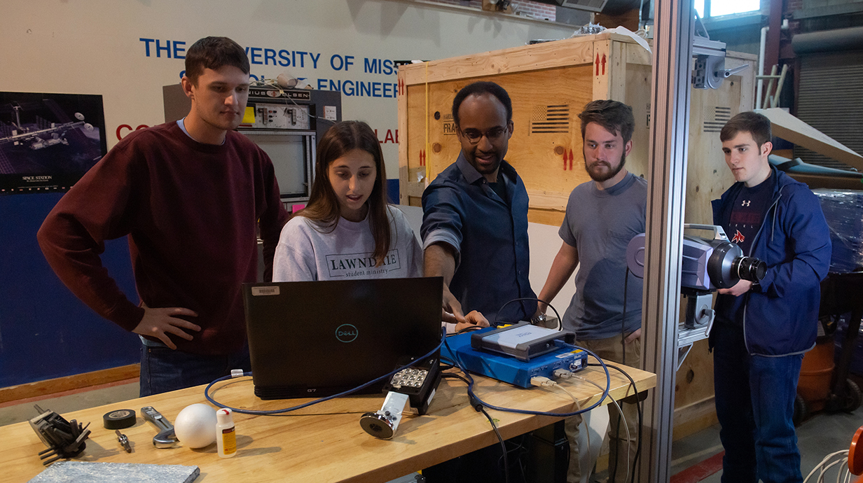 Four college students and a professor work with computer equipment in an engineering lab.