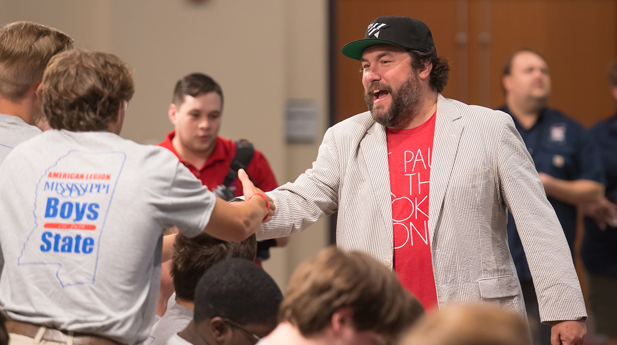 A bearded man wearing a sportcoat shakes hands with a student wearing a Boys State T-shirt.