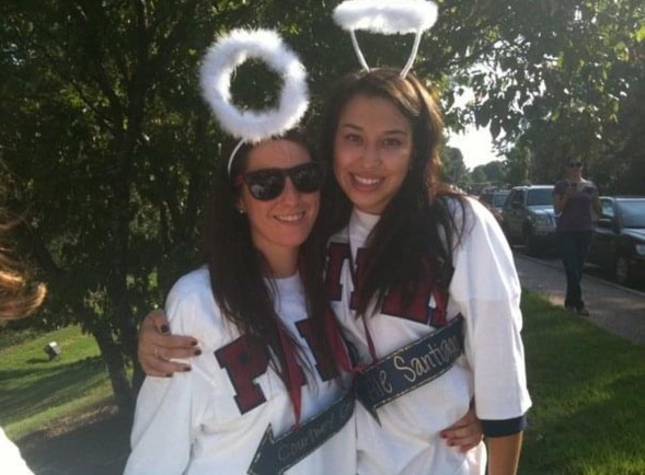 Two women wearing T-shirts and fuzzy headpieces stand outside.