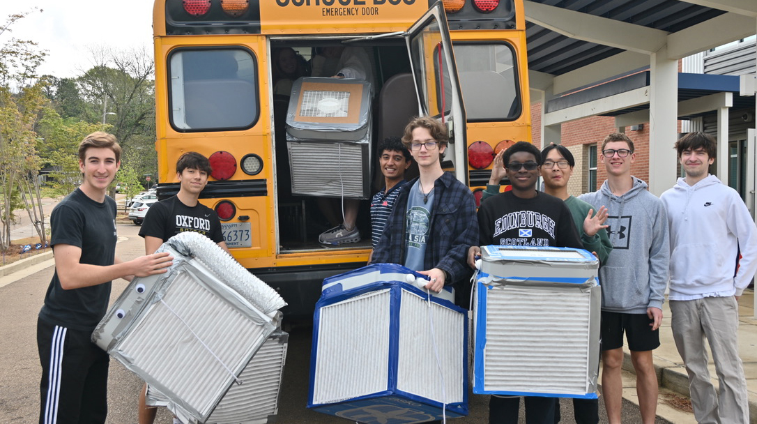 Several young men unload air filters from the back of a school bus.