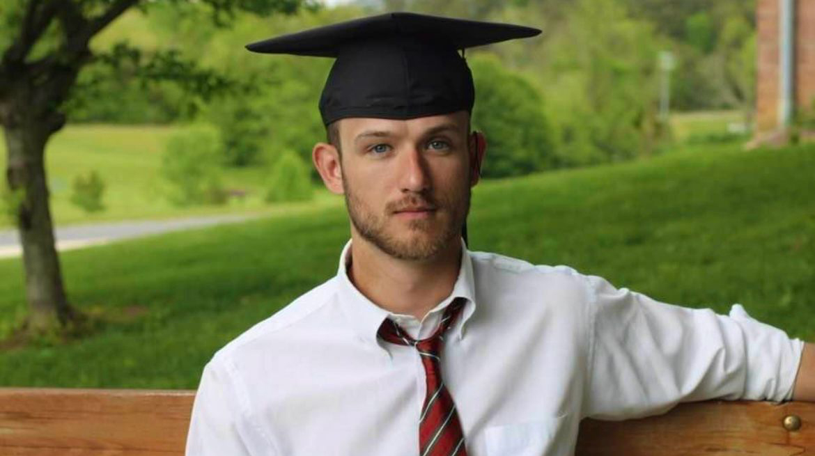 A man wearing a white shirt and a graduation cap poses for a photo.