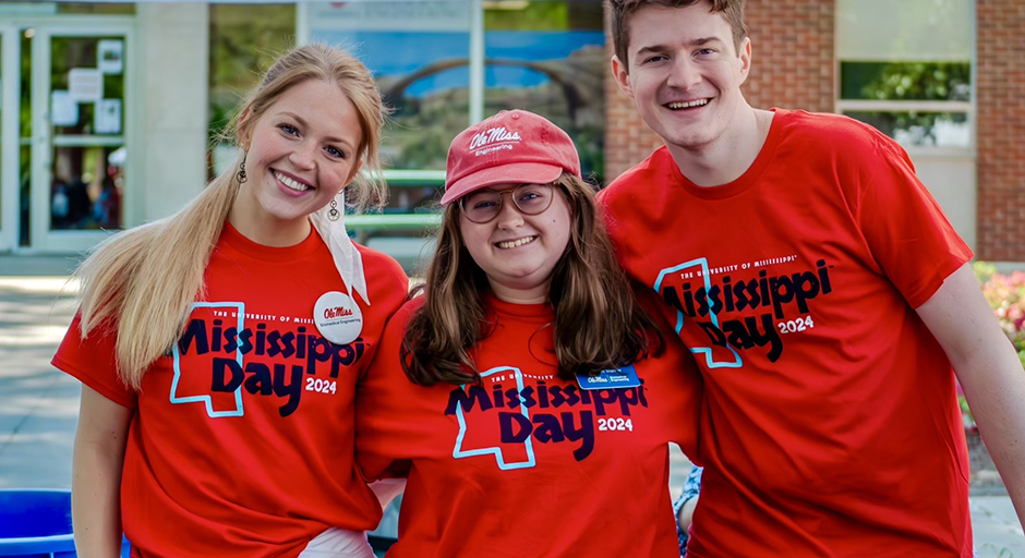 Three young people wearing red Mississippi day T-shirts stand at a table outdoors.