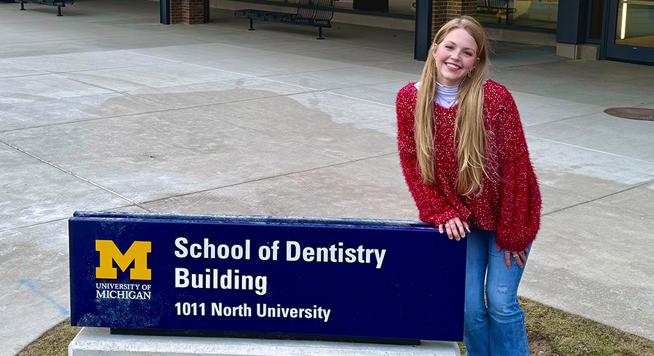 A young woman sits on a concrete sign reading 'School of Dentistry Building.'