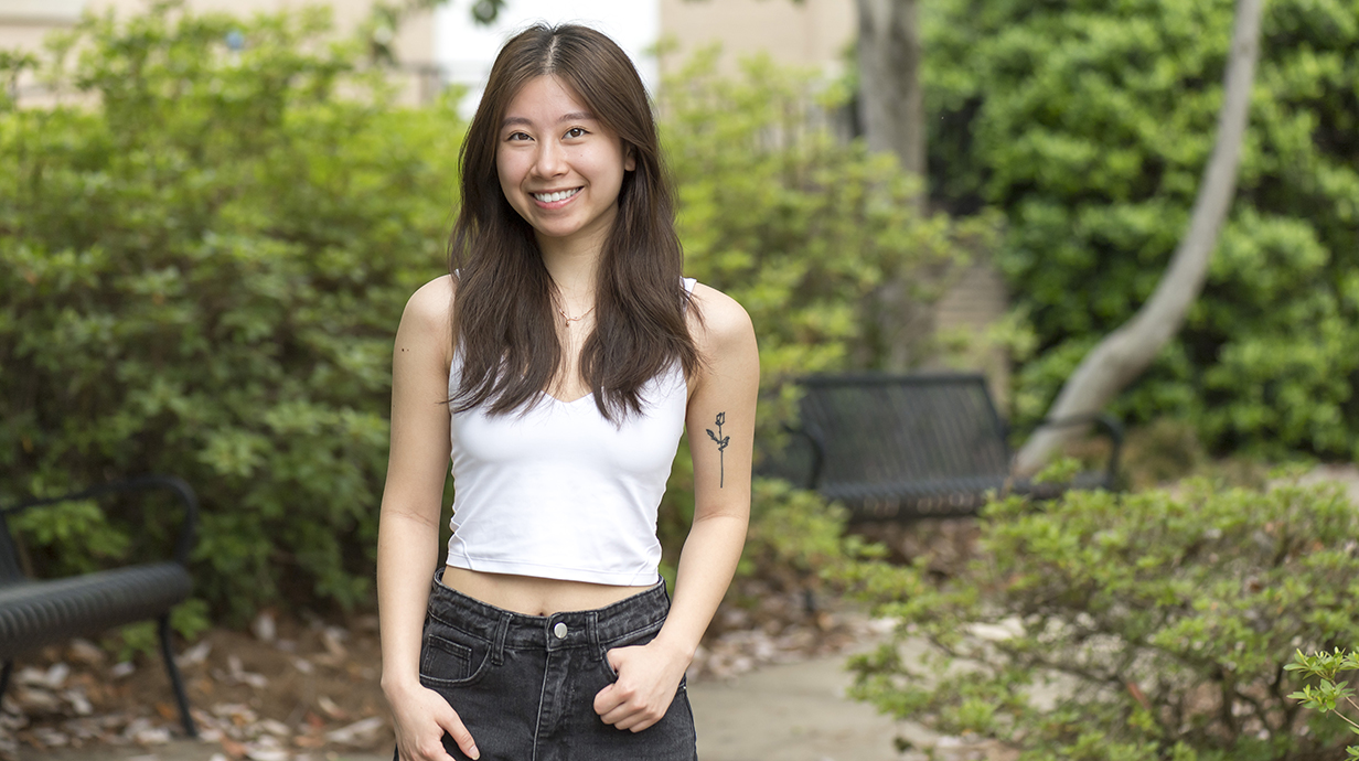 A young woman stands outside, with her hands hanging loosely from her jeans pockets.