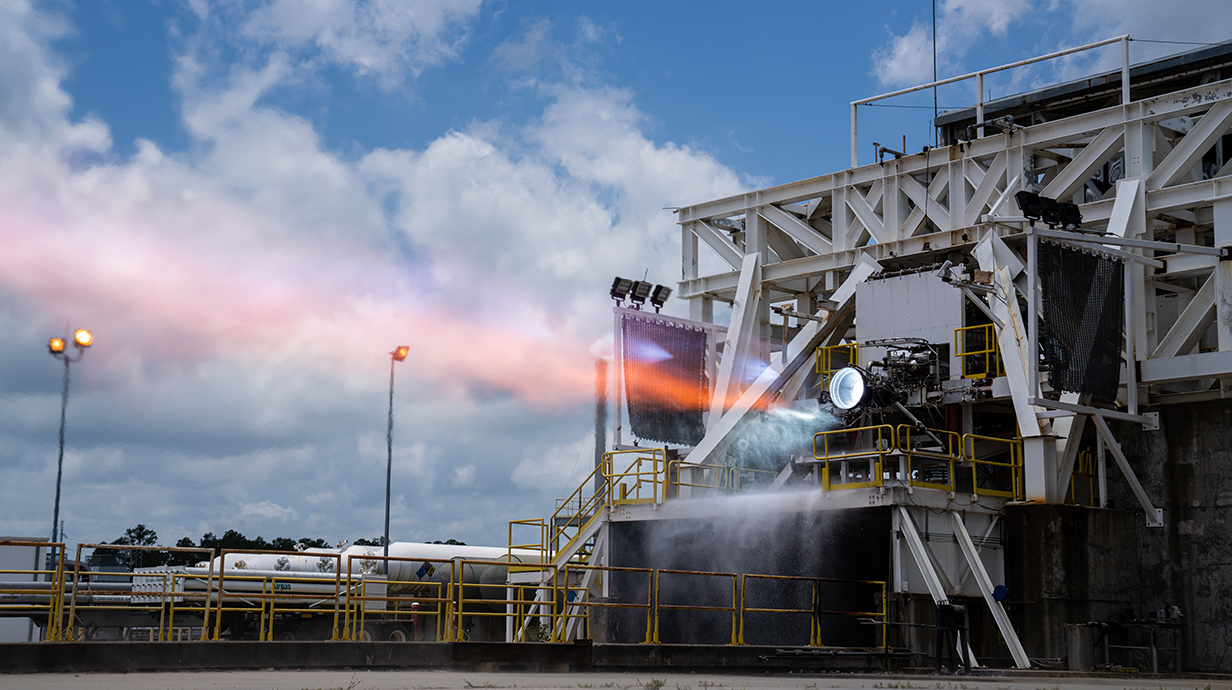 A rocket engine being test-fired shoots flames out of a tower structure.