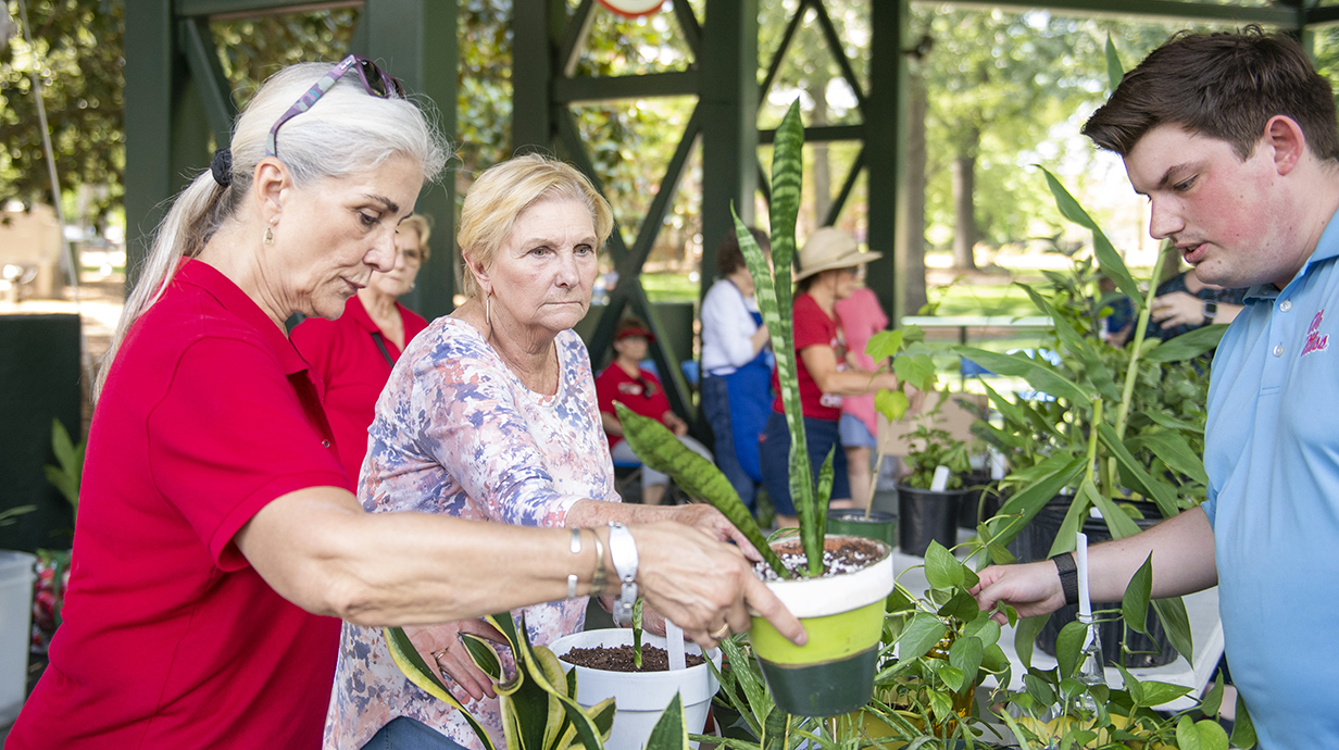 Two women and a man sort through potted plants on a stage.