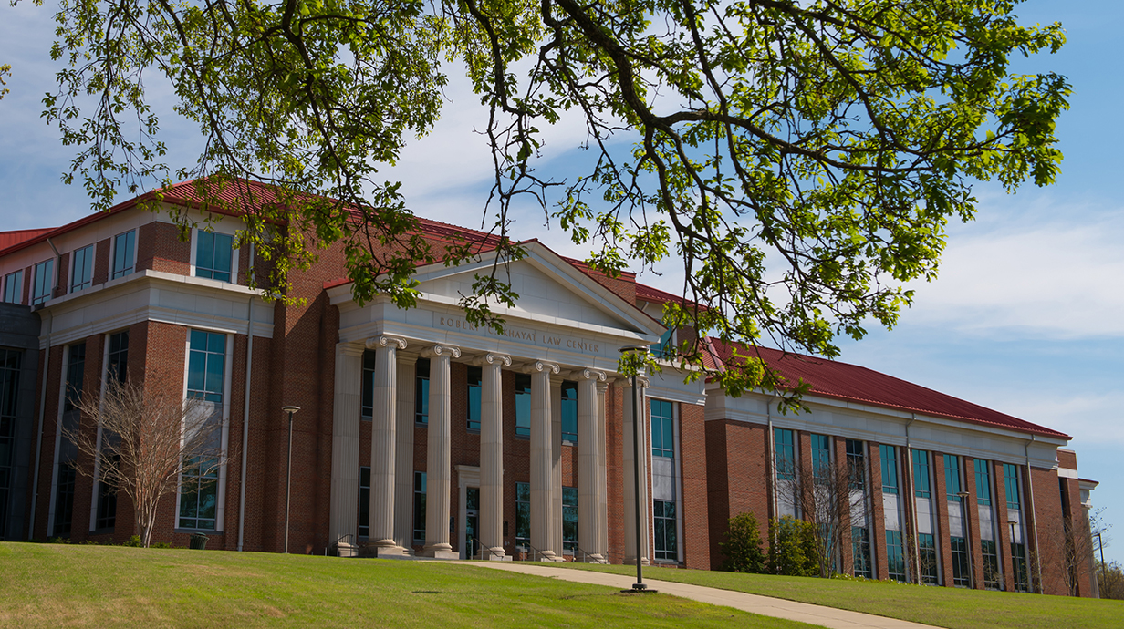 A red brick building with a columned facade sits atop a hill.