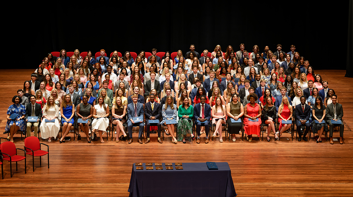 A group of more than 200 young people sit in chairs on a stage.