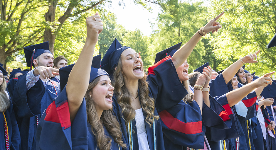 A group of young women wearing graduation robes cheer.