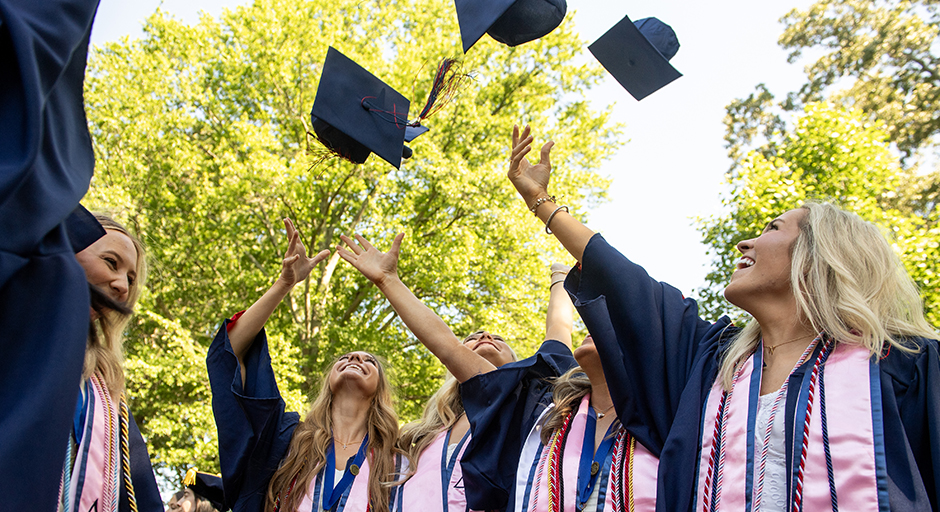 A group of young women wearing graduation robes toss their caps into the air.