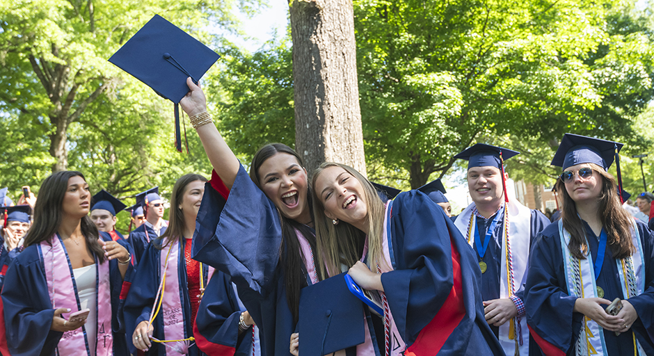 A group of young college graduates celebrate in a park.