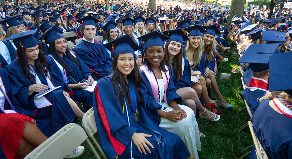 A group of young people wearing graduation robes sit in a park.