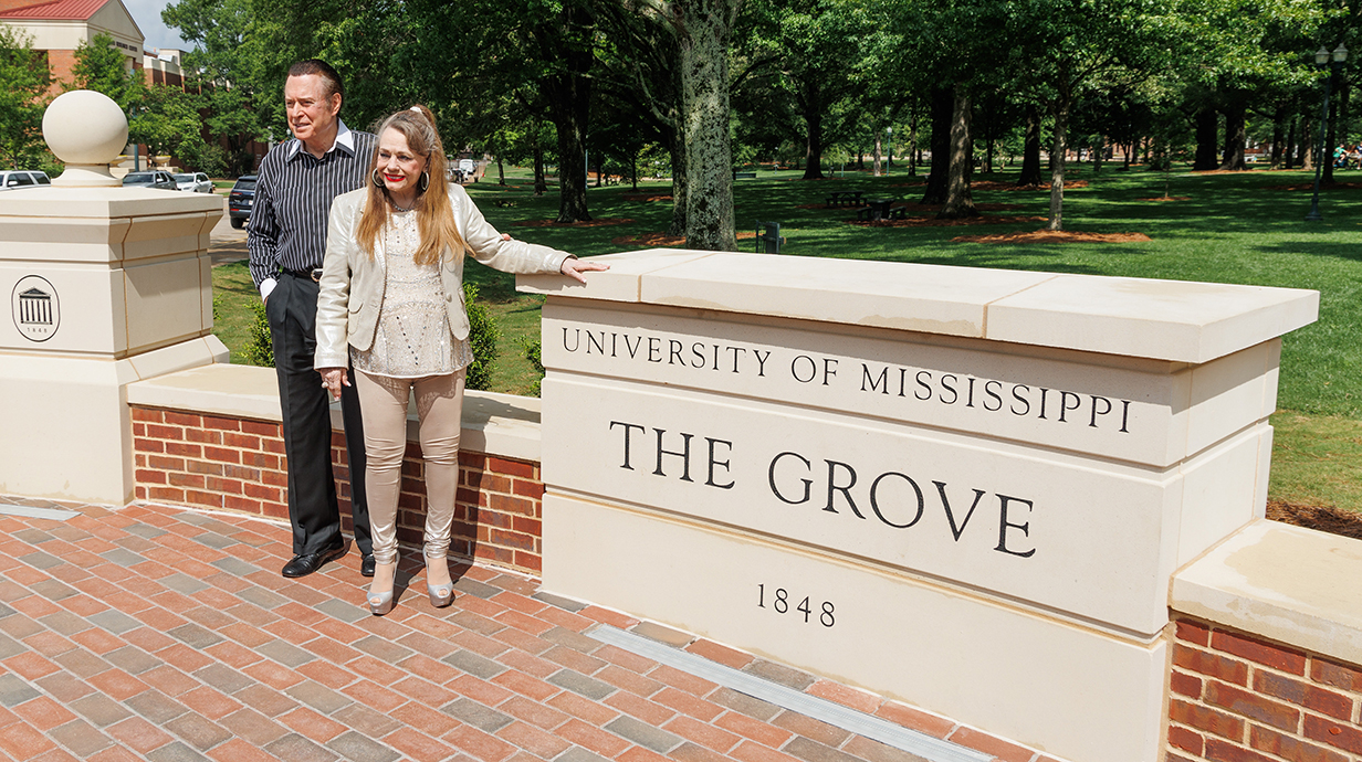 A man and woman stand on a brick plaza at a park beside a concrete sign reading "The Grove."