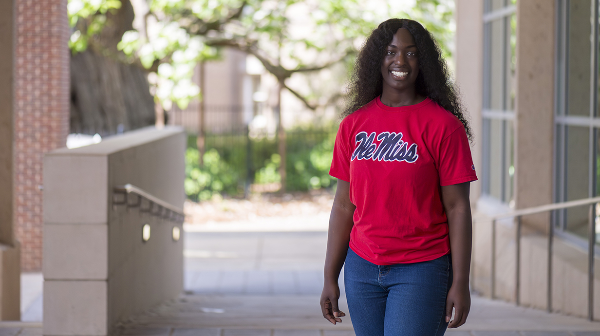 A young woman wearing a red Ole Miss T-shirt stands underneath a brick patio.