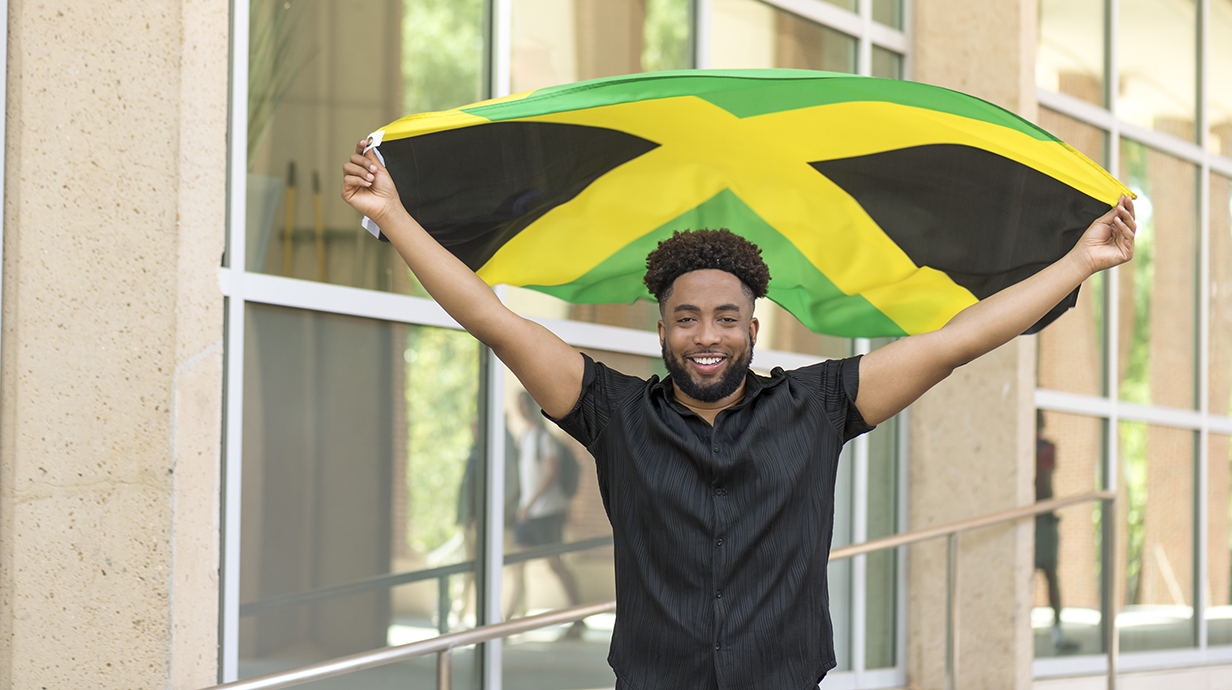 A young man holds a green, yellow and black flag above his head on an outdoor plaza.