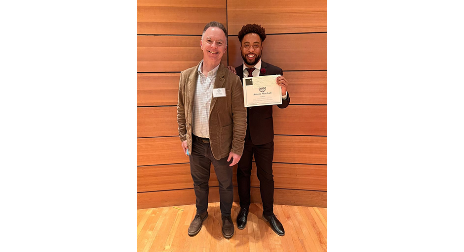 A young man holding an award certificate stands next to an older man.
