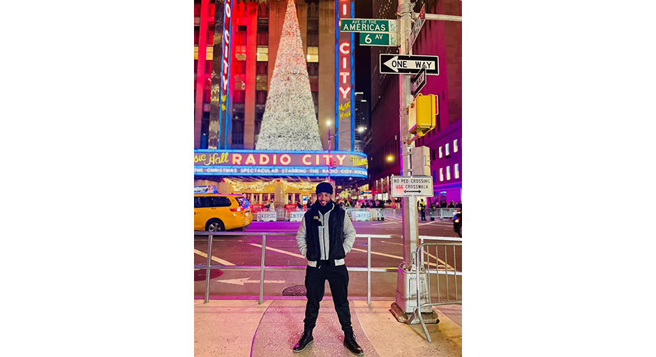 A young man stands on a brightly lit street in front of Radio City Music Hall in New York.