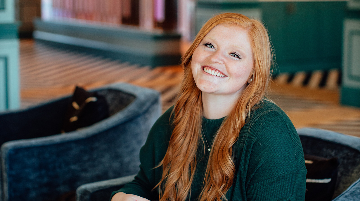 A young woman in a green dress sits in a hotel lobby.