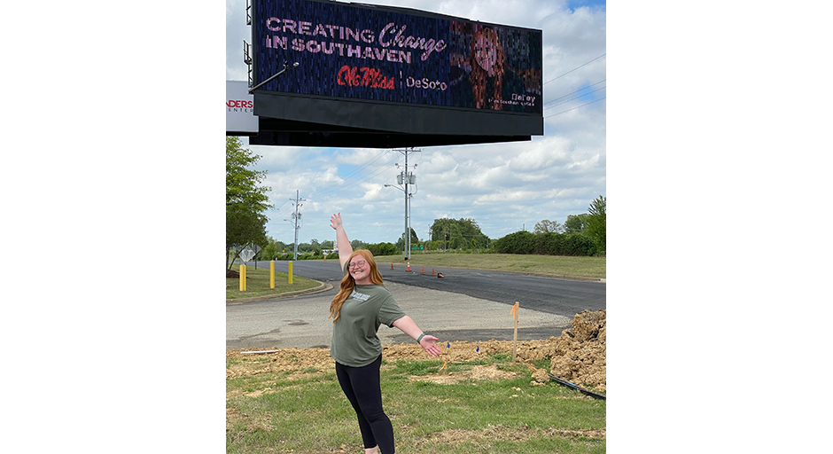 A woman stands underneath an electronic billboard.