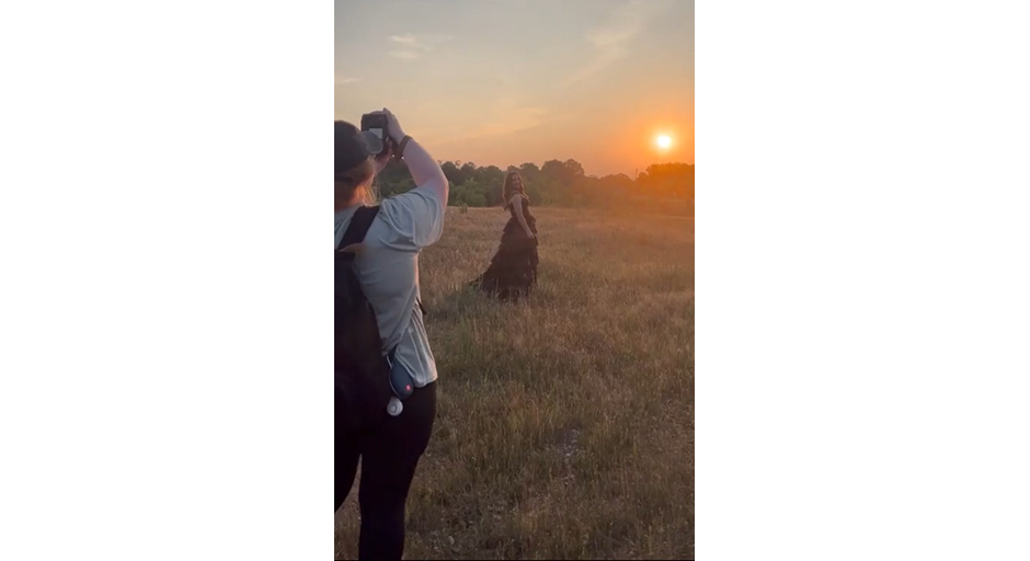 A photographer shoots a picture of a woman in front of a beautiful sunset.