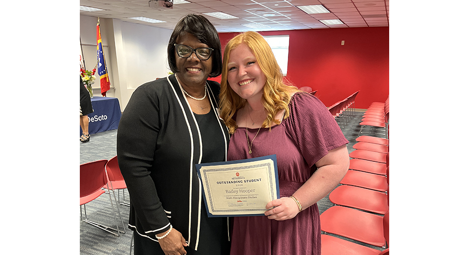 A woman congratulates a young woman holding an award certificate.