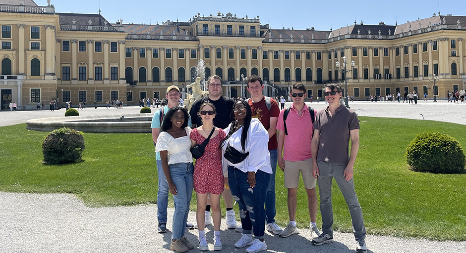 A group of young people stands outside a palace.