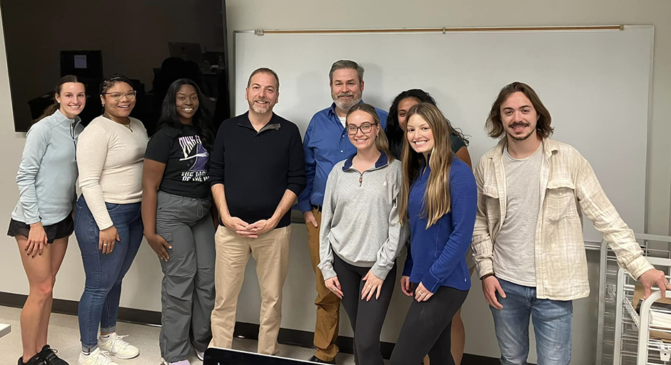 A group of people stands against the wall of a classroom for a group photo.