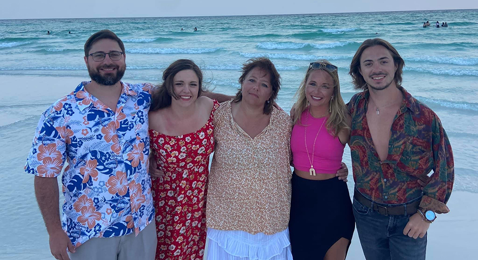 A family takes a group photo at a beach.
