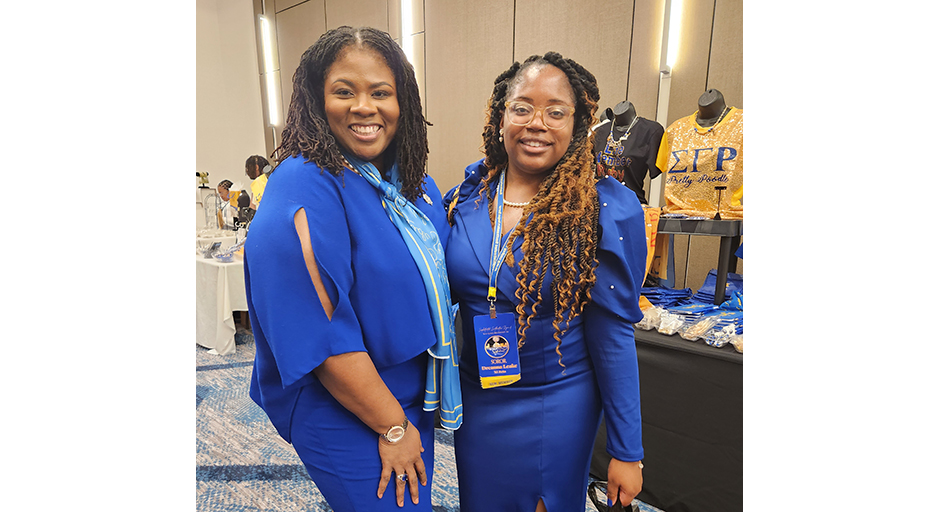 Two women in blue dresses stand in a conference hall.