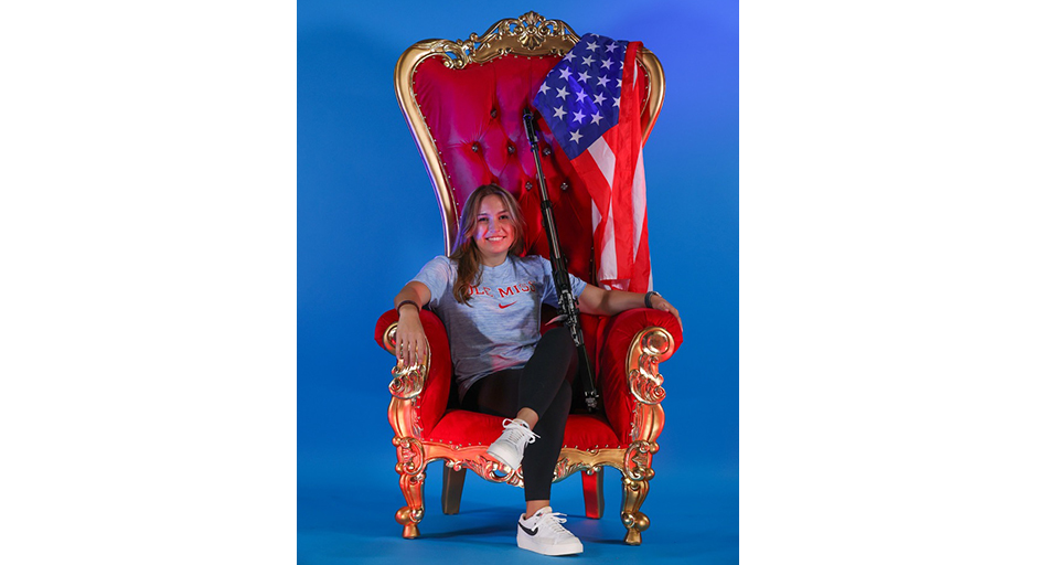 A young woman sits in a large, ornate red and gold chair.