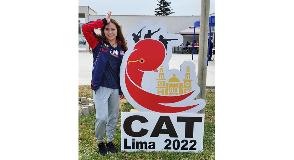 A young woman stands behind a sign for a shooting competition in Lima, Peru.