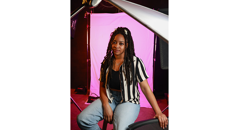 A young woman sits in front of a background screen in a photo studio.