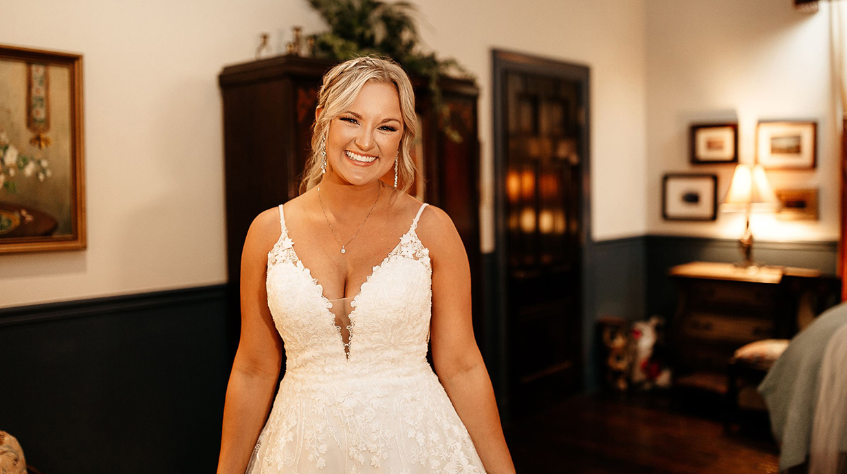 A woman wearing a wedding dress stands in a living room.