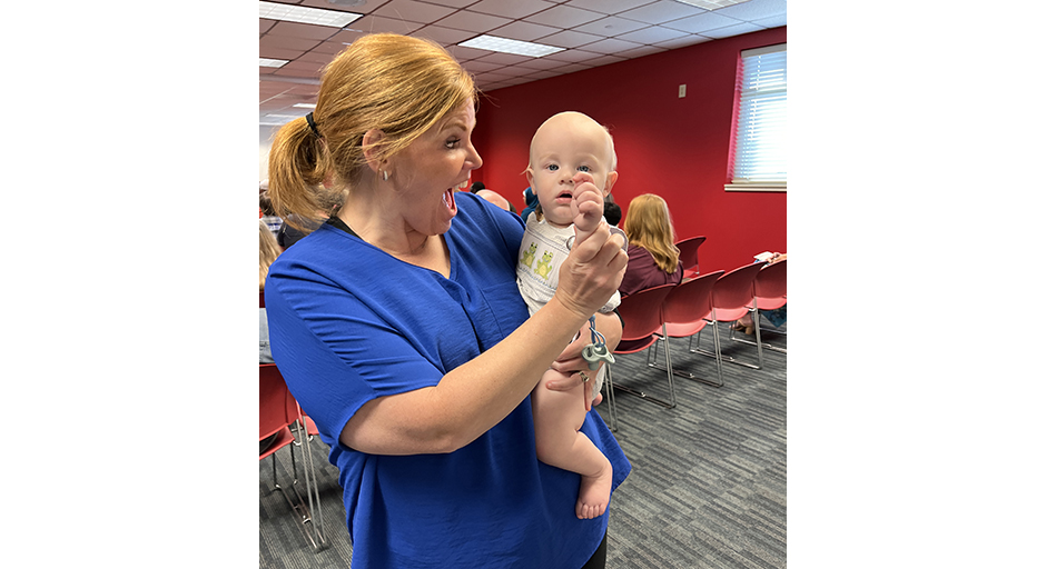 A woman in a blue shirt holds a baby boy.