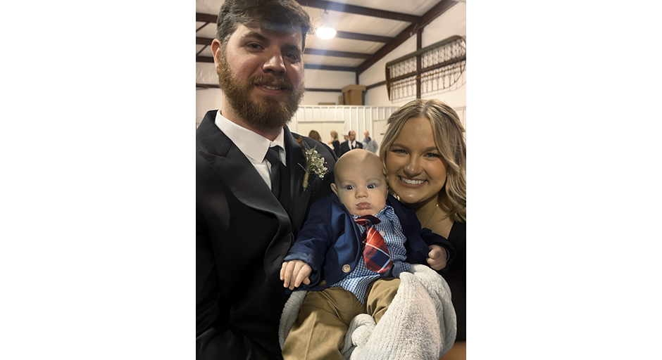 A man and a woman hold a baby wearing a necktie.