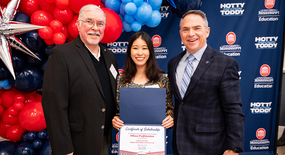 Two men present an award certificate to a young woman.