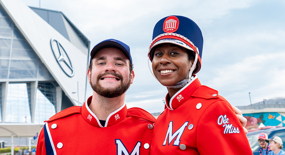 Two band members in red uniforms stand outside a stadium.
