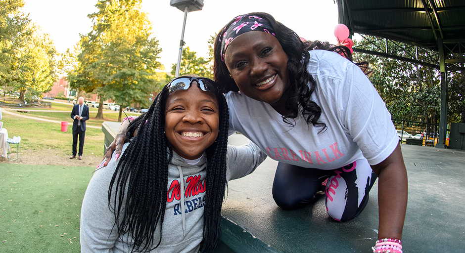 Two women embrace and smile at the edge of an outdoor stage.