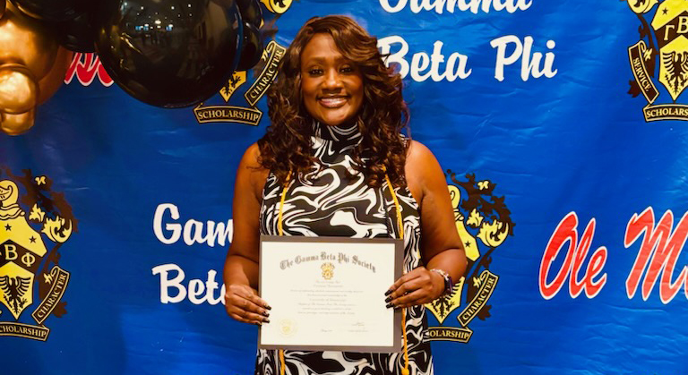 A woman holds an award certificate in front of a bright blue banner.