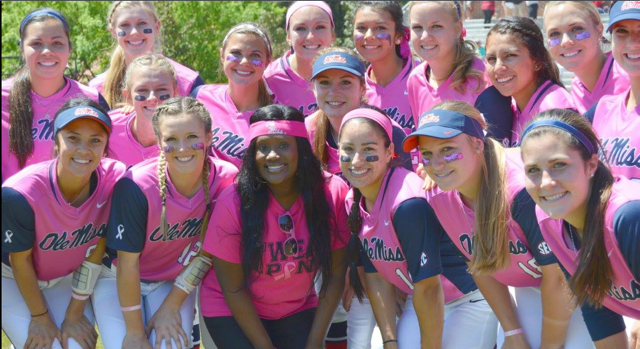 A women's softball team, all dressed in pink jerseys, poses for a photo.