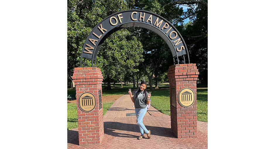 A young woman stands underneath an outdoor archway reading Walk of Champions.