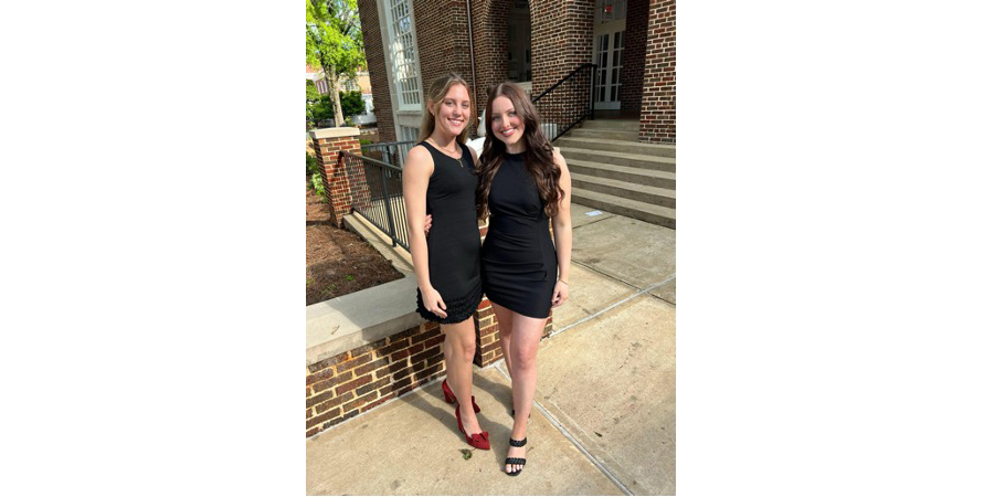 Two young women in black dresses pose for a photo.