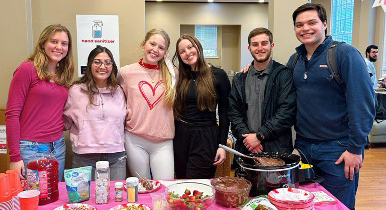 A group of young people stands behind a party table decorated in pink.