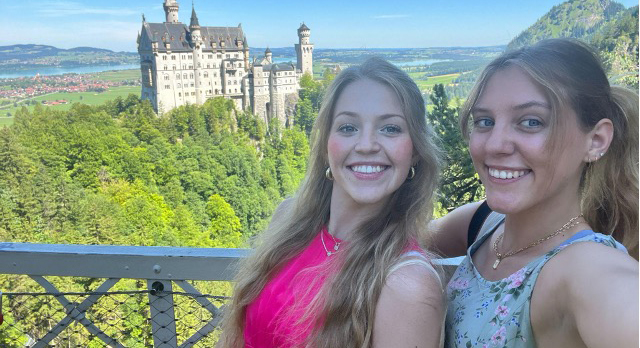 Two young women take a selfie in front of a castle.
