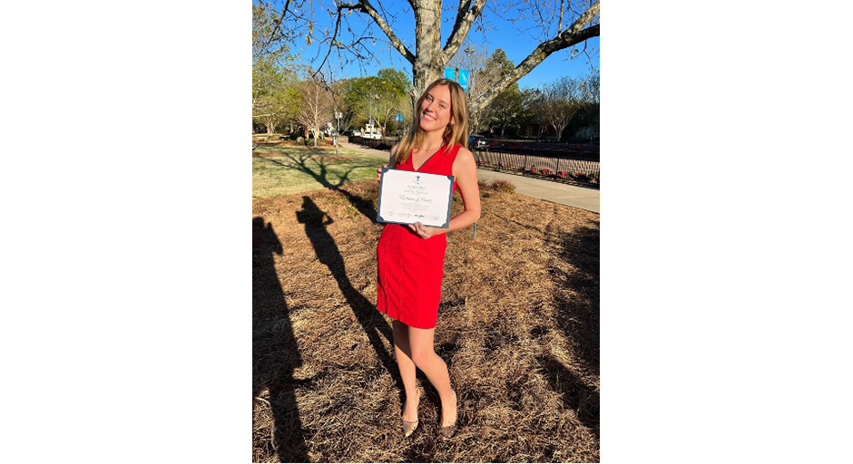 A young woman in a red dress holds an award certificate.