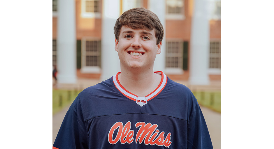 A young man wearing a blue Ole Miss jersey stands in front of a white-columned building.