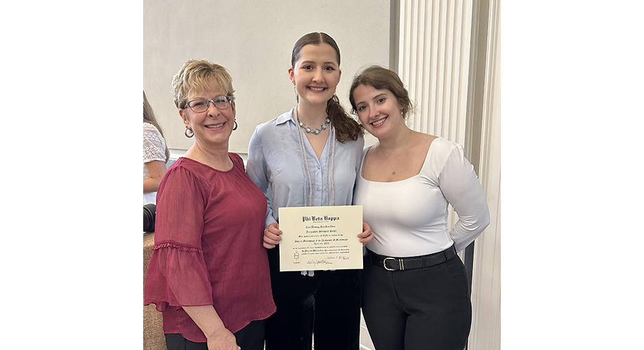 Three women, the center one holding an award certificate, pose for a photo.