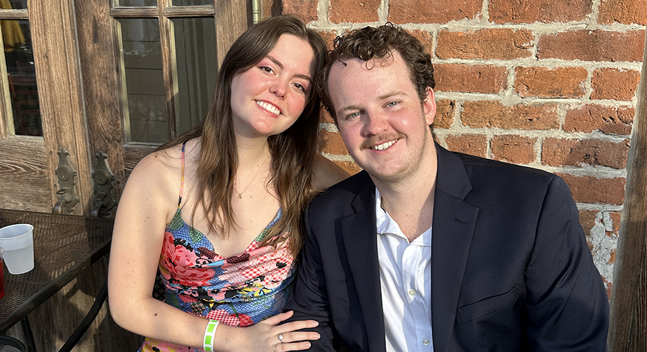 A young woman and man sit on a bench outside a brick building.