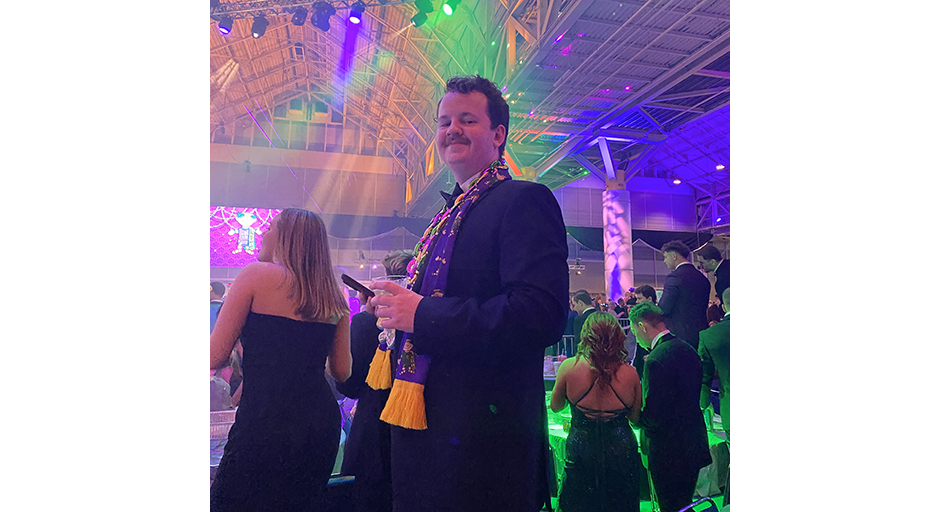 A young man wears a tux and a purple scarf at a formal ball.